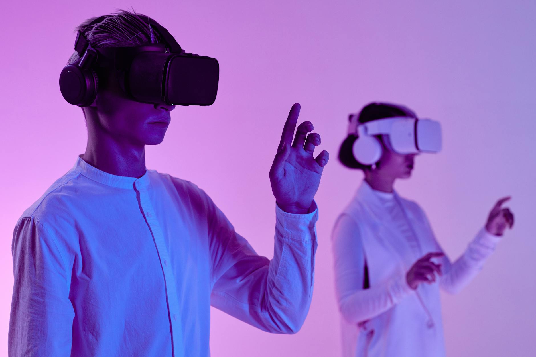 Two people engage in a futuristic virtual reality simulation with headsets and vibrant lighting. (Photo by Michelangelo Buonarroti on Pexels)